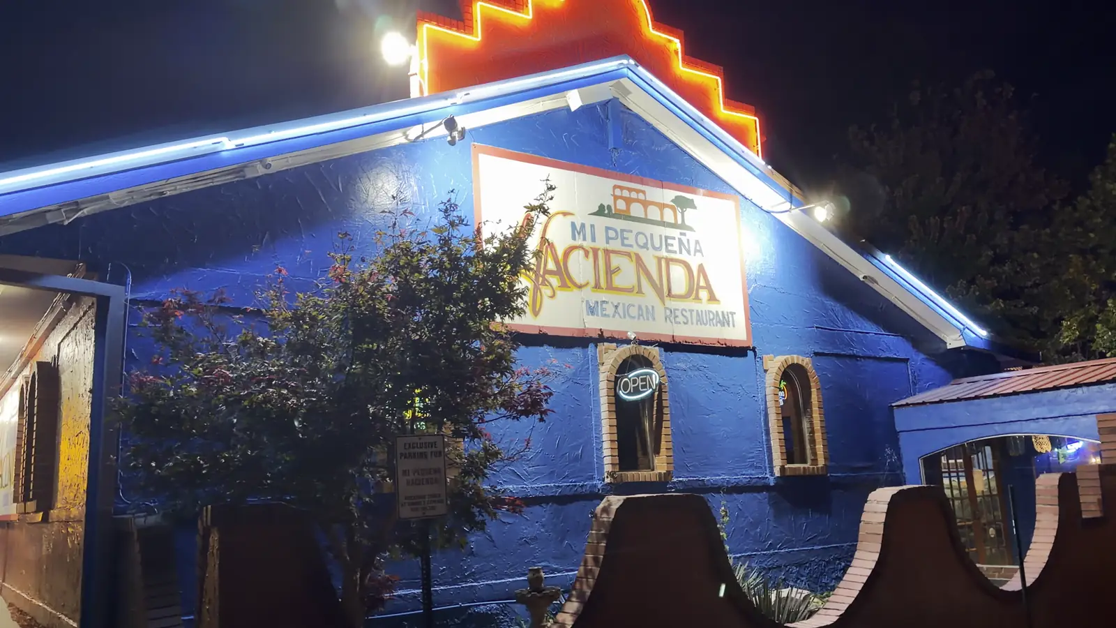 The cobalt-blue Mi Pequeña Hacienda building at night, with its stepped orange neon roofline and hand-painted sign